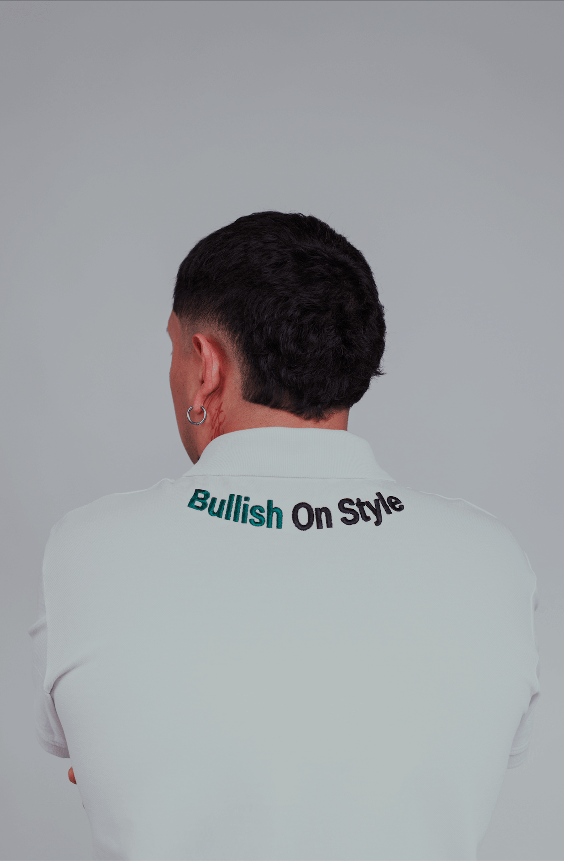 Man wearing BOS-BBS-100 Polo with "Bullish On Style" embroidered on back, showcasing limited edition design in white.